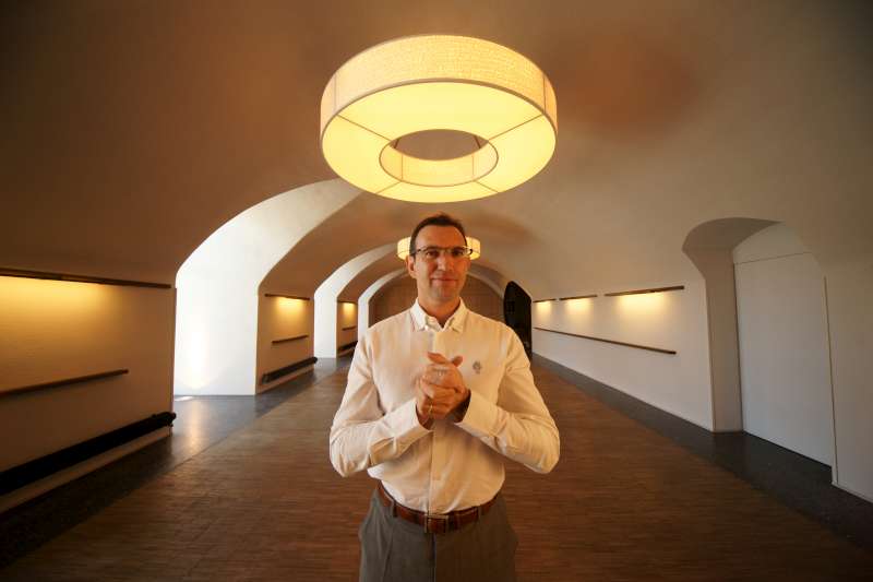 Frédéric Panaiotis - Ruinart. Champagne Ruinart has monastic origins and to reflect this Frédéric stands with his hands clasped. He is in the new dinning room at Ruinart which has circular lights, one of which is positioned like a halo. The dining room has been designed to mirror the shape of the cellars below.